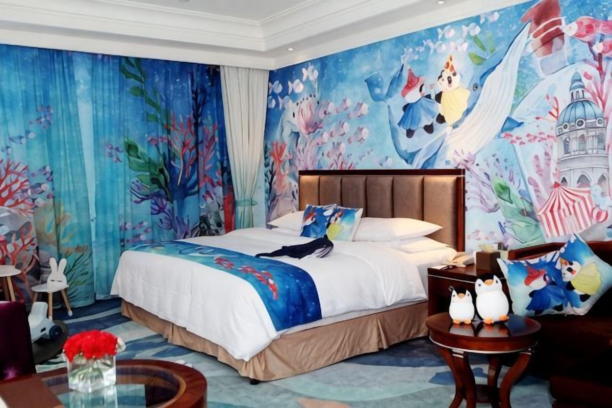 A hotel room with a large bed, a mural on the wall, and a round table with decorative items.