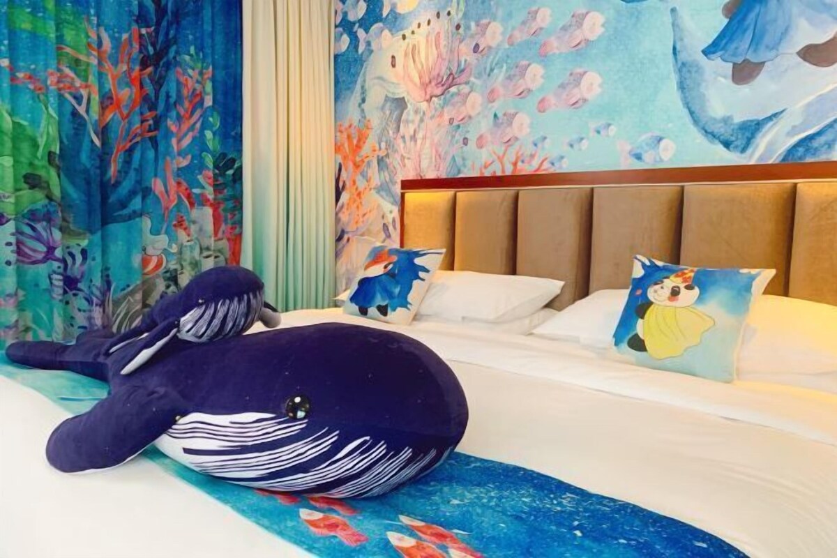 Una camera d'hotel con un letto, un'ampia decorazione a forma di balena e un colorato murale con scene subacquee.