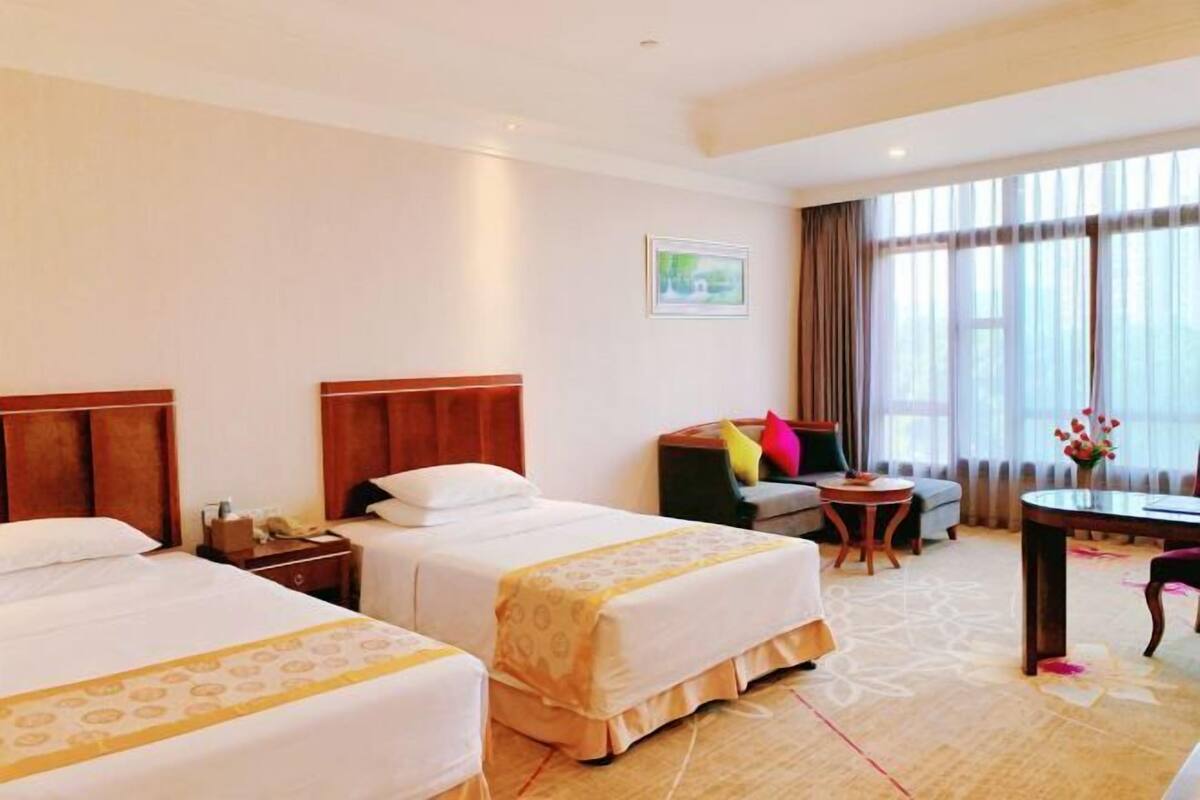 A hotel room with two beds, a desk, a chair, a small table, and a window with curtains.