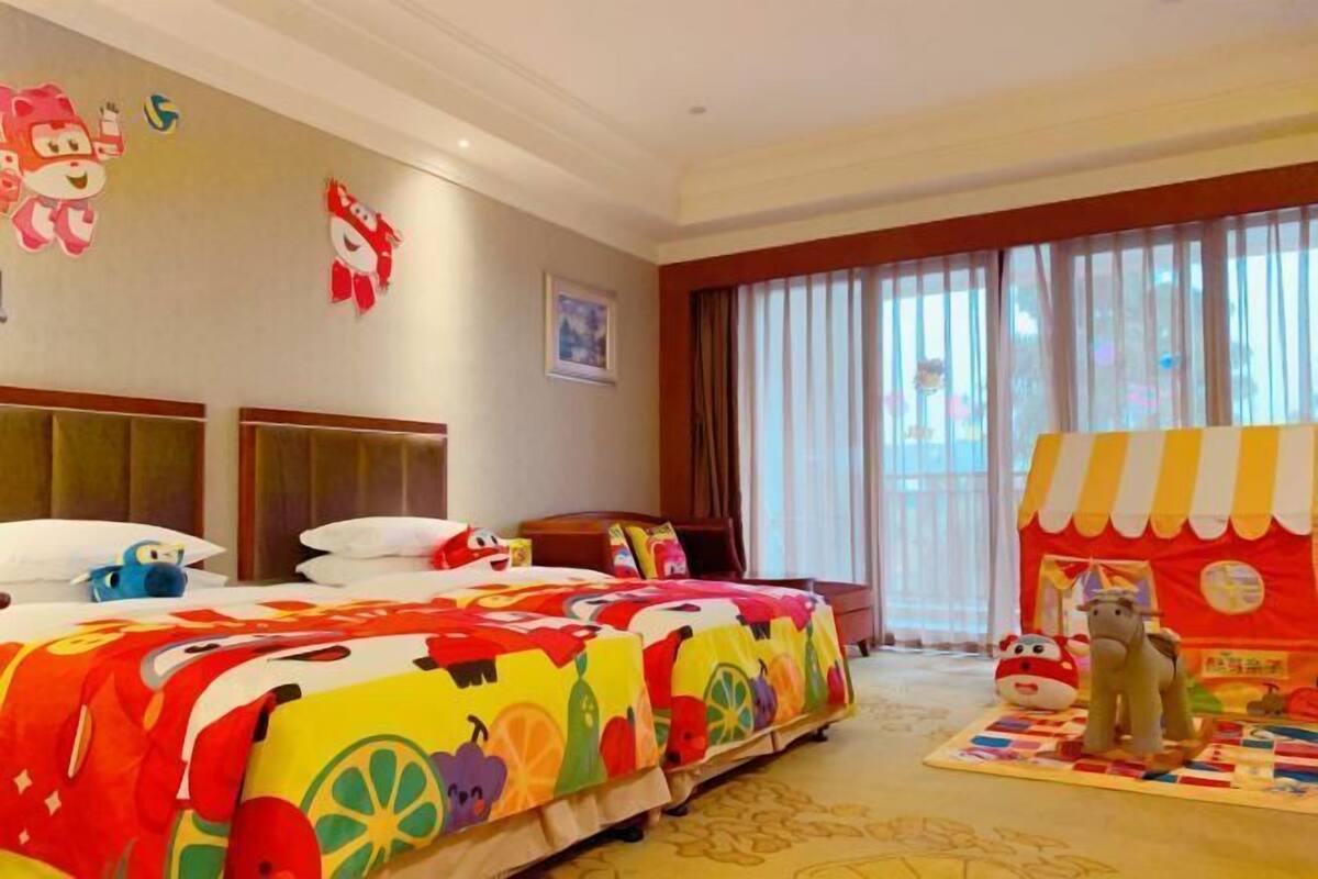 A hotel room with a large bed, a small table, and a play area with toys.