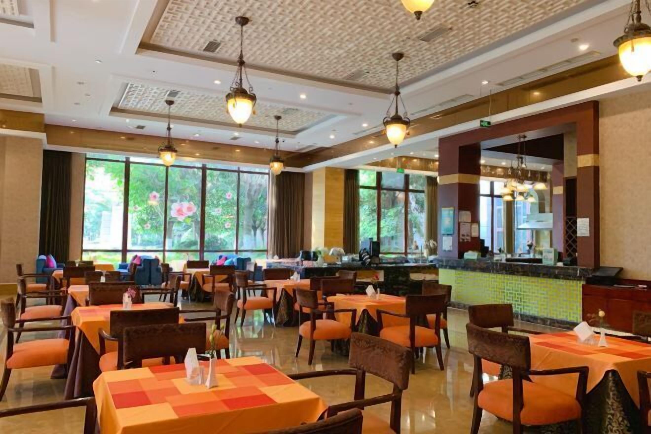 Un espace de restauration d’hôtel avec des tables et des chaises, un comptoir où est affiché le menu, et de grandes fenêtres donnant sur un paysage verdoyant.