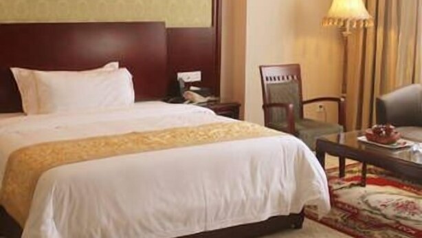 A hotel room with a large bed, a chair, a table, and a lamp. - Vienna Hotel Huizhou Zhongkai Avenue (Huizhou)