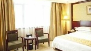 A hotel room with a bed, two chairs, a small table, and a lamp. - Vienna Hotel Huizhou Zhongkai Avenue (Huizhou)
