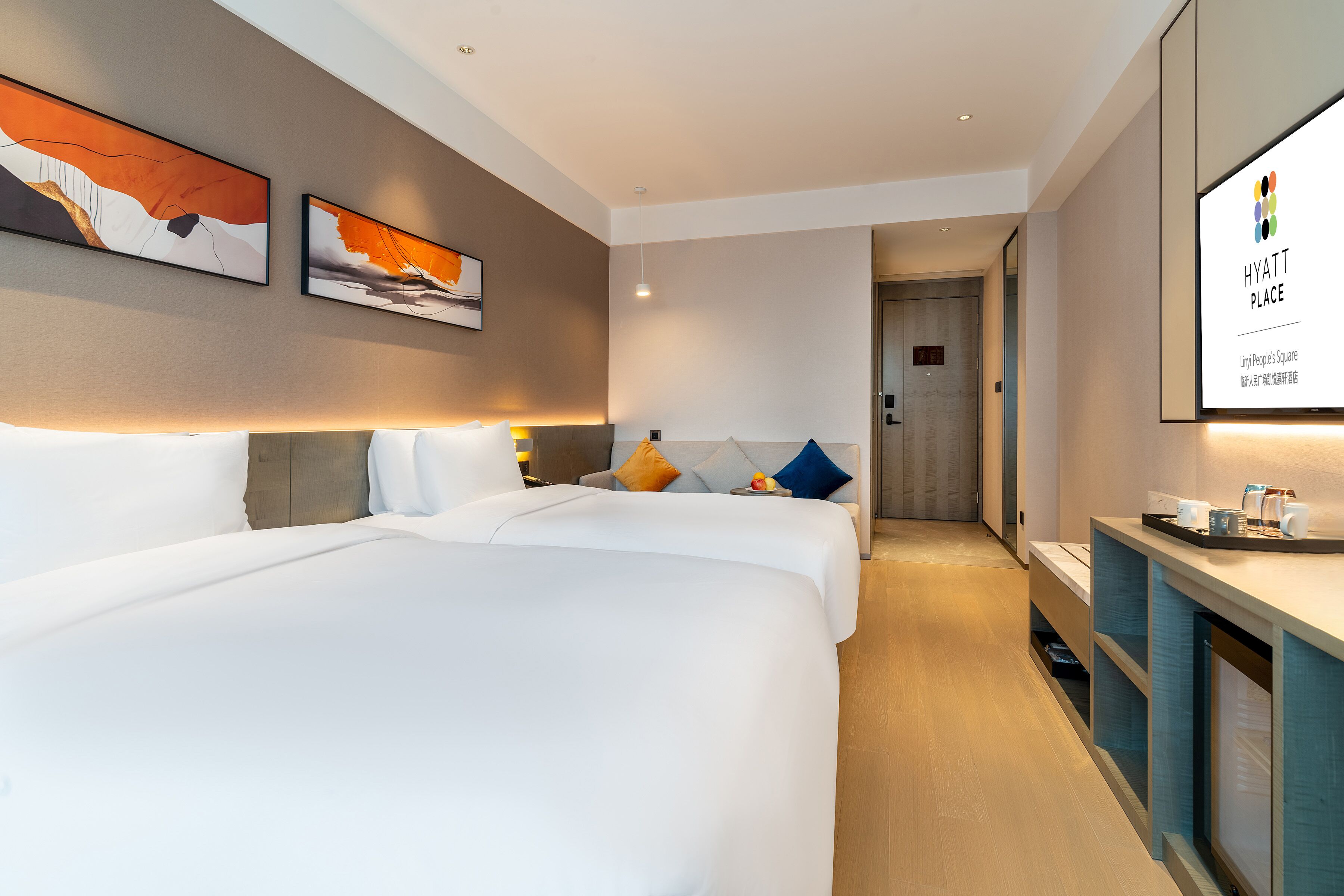 Une chambre d’hôtel avec deux lits, un bureau et des œuvres d’art accrochées aux murs.