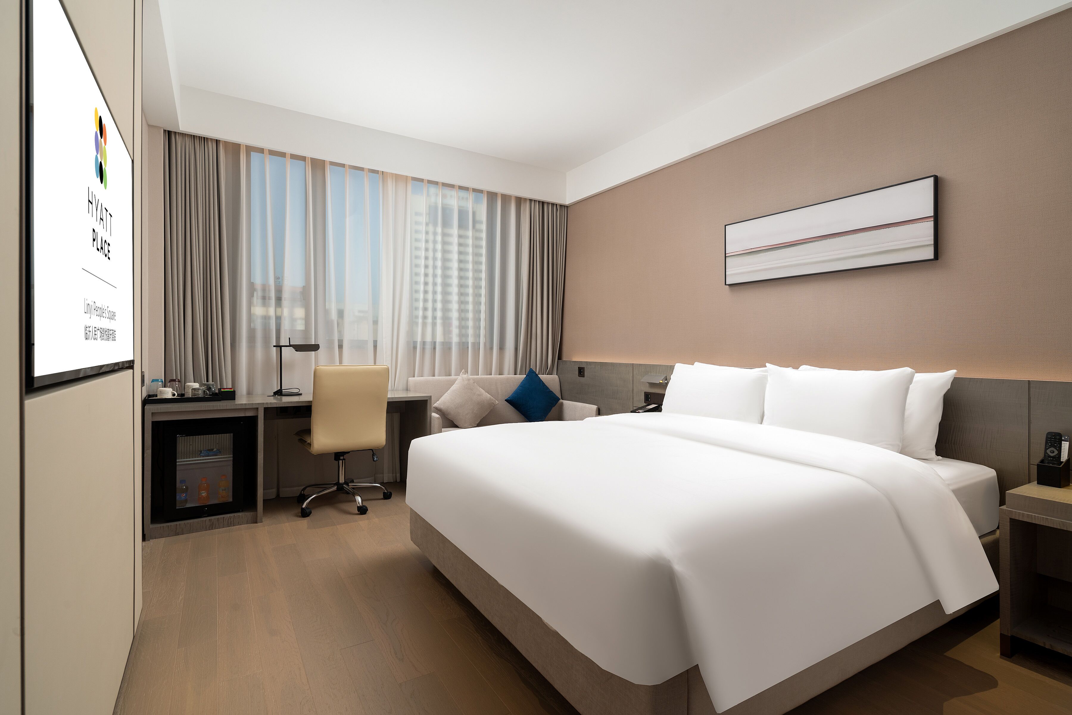 A modern hotel room with a large bed, a desk with a chair, a small table, and a large window with curtains.