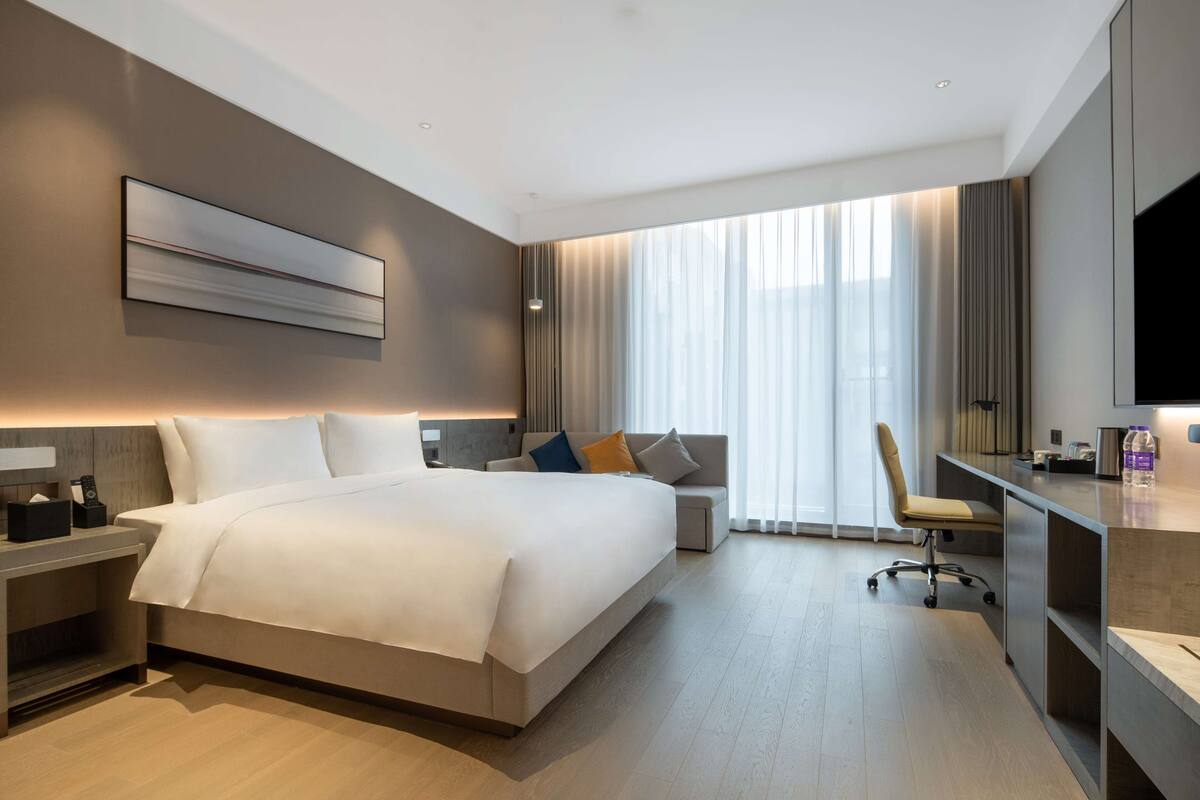 A modern hotel room with a large bed, a desk, a chair, and a TV.