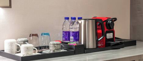 A hotel room's coffee station with a coffee maker, water bottles, and mugs.