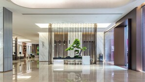 Un vestíbulo moderno con un mostrador de recepción central, una gran planta en maceta y un suelo liso y reflectante.