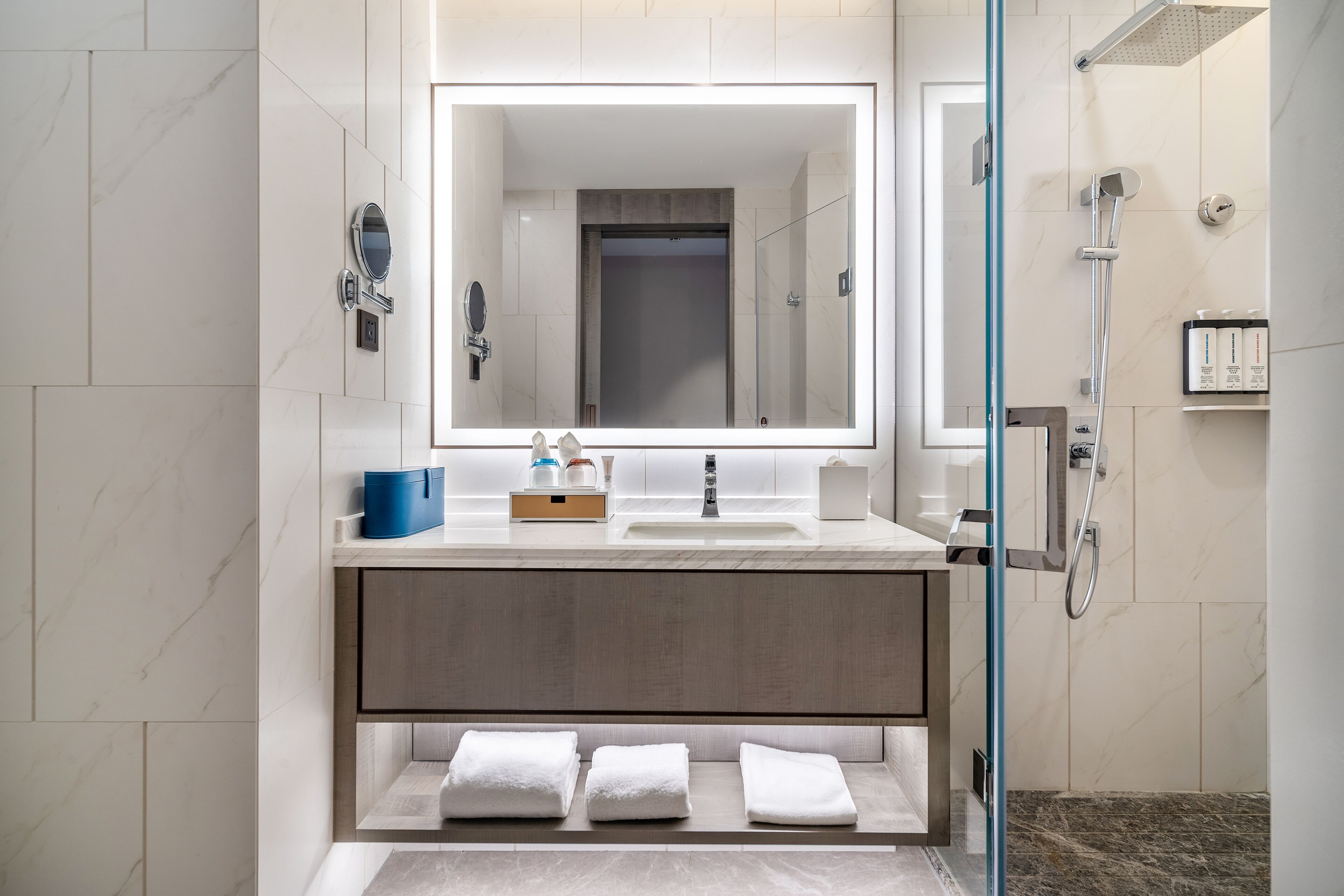A modern bathroom with a large mirror, a shower, and a vanity with towels.