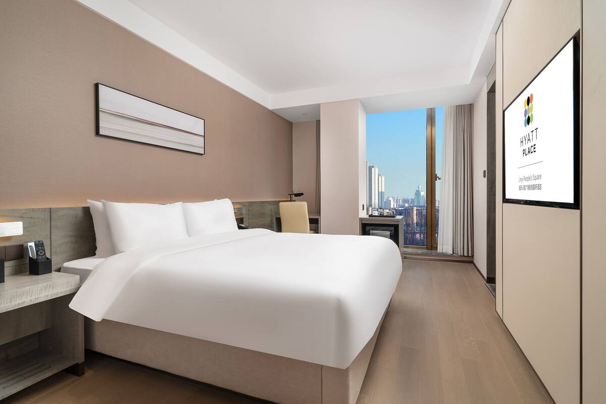 A modern hotel room with a large bed, a desk, and a city view.