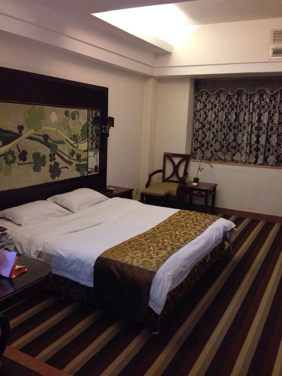 Une chambre d’hôtel avec un lit, une chaise, une petite table et une fenêtre avec des rideaux à motifs.