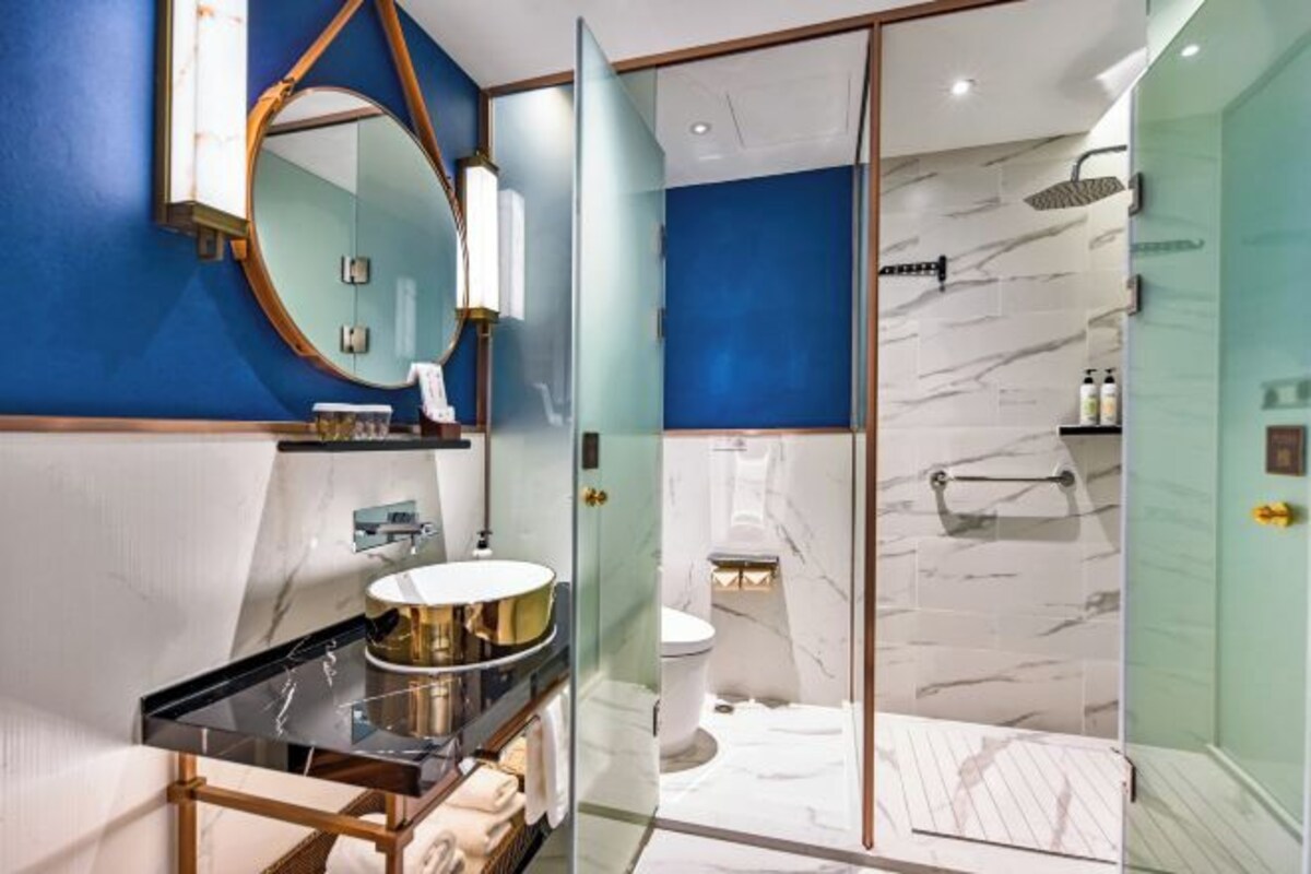 Un baño moderno con cabina de ducha de vidrio, un espejo redondo y zona de ducha con azulejos de mármol.
