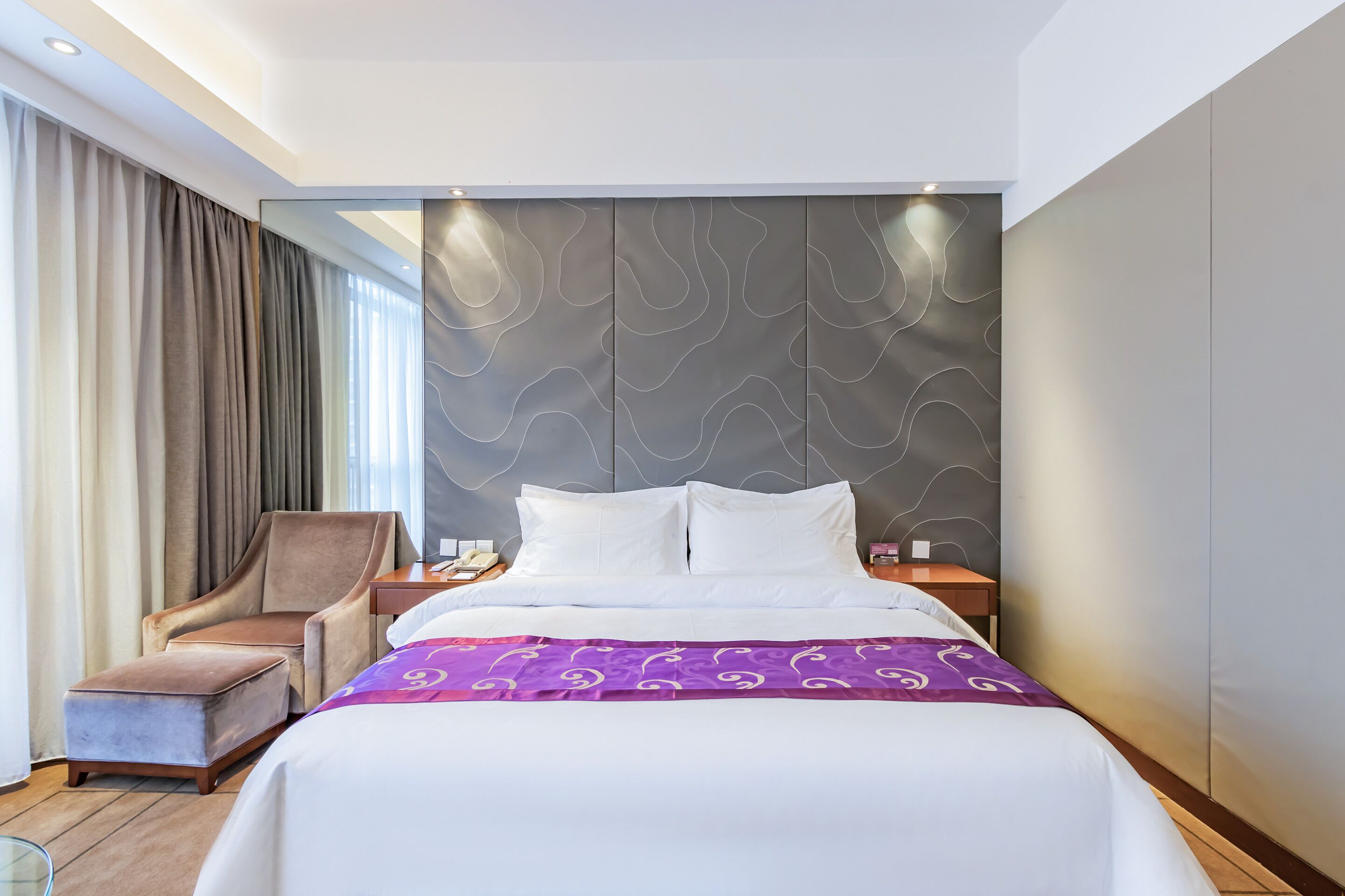 A hotel room with a bed, a chair, a nightstand, and a wall with a wavy pattern.