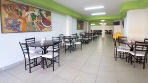 Un comedor con varias mesas y sillas, paredes pintadas de verde y obras de arte en las paredes.