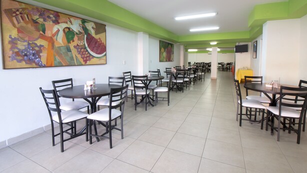 A dining area with multiple tables and chairs, green painted walls, and artwork on the walls. - CHN Hotel Monterrey Santa Fe (Monterrey)