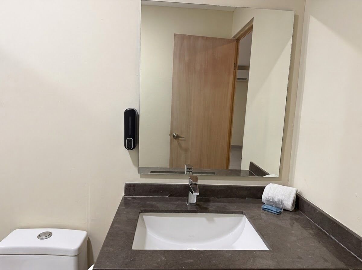 Une salle de bain avec un lavabo blanc, un miroir et une porte à l’arrière-plan.