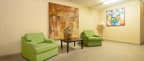 A waiting area with two green armchairs, a coffee table, and two artworks on the walls.