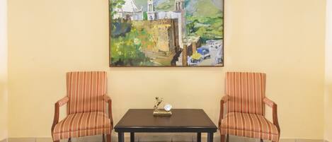 Une pièce avec deux fauteuils à rayures, une petite table et un tableau représentant une église et des montagnes accroché au mur.