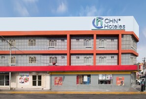 Un hotel de varios pisos con un llamativo letrero de CNH Hotels, que presenta un dise ño arquitectónico moderno con fachada roja y gris.