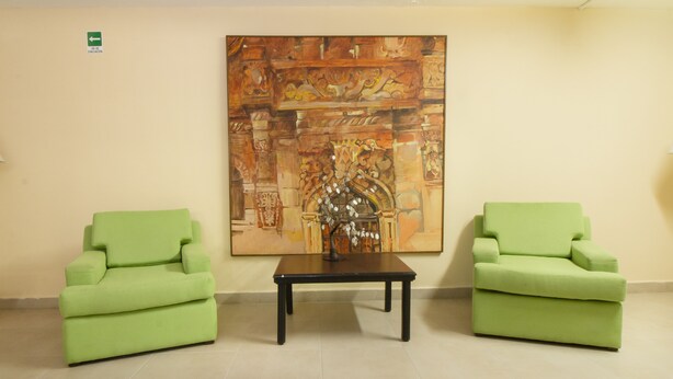 Una habitación con dos sillones verdes y una mesita, con un cuadro grande en la pared.