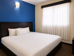 A hotel room with a single bed, a dark headboard, a wall-mounted light, and a window with sheer curtains. - CHN Hotel Monterrey Santa Fe (Monterrey)