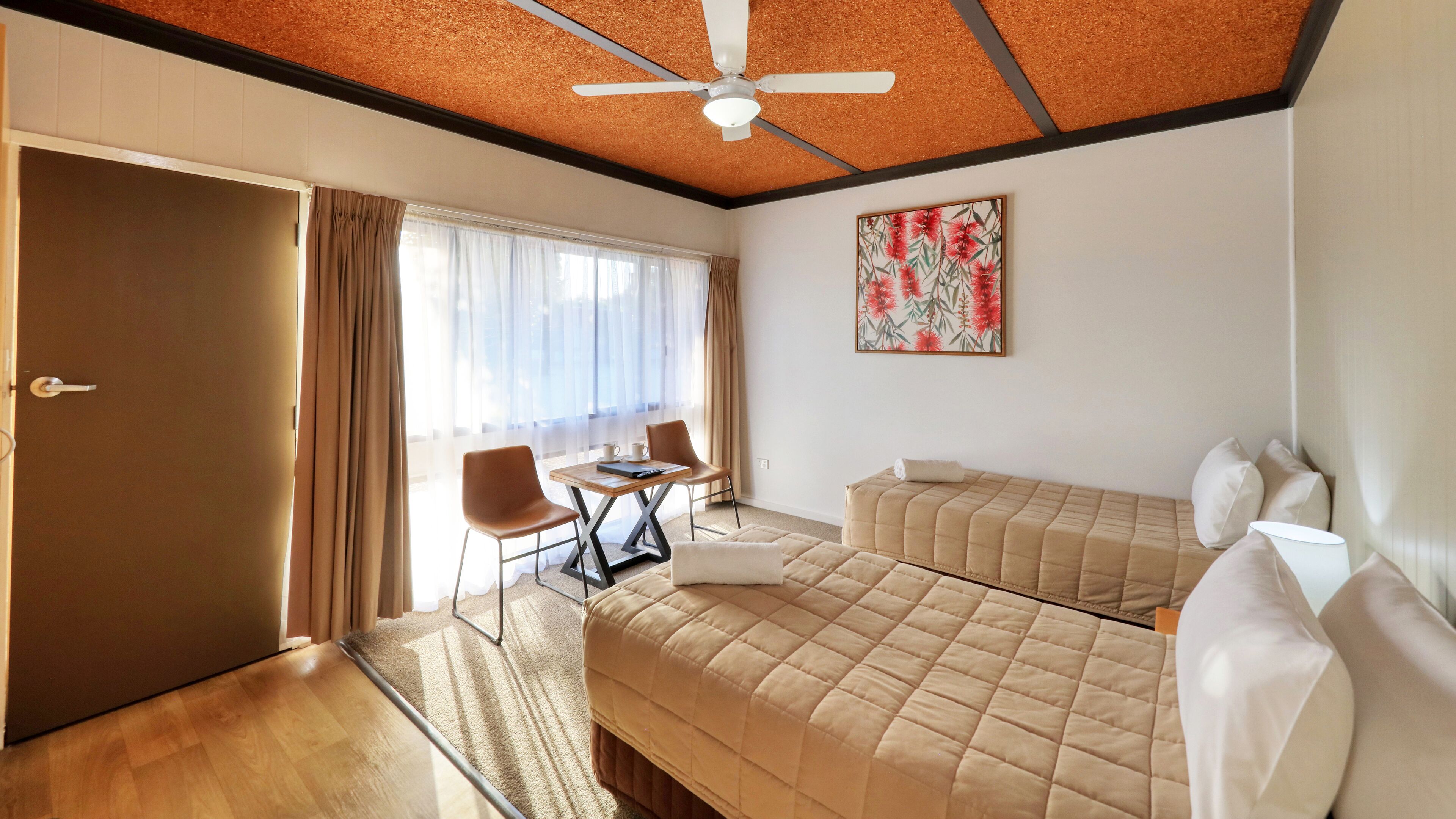 A hotel room with a bed, a desk, a chair, and a ceiling fan.