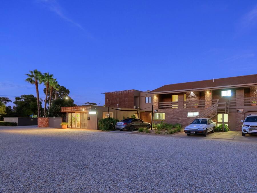 A two-story house with a driveway, three cars parked, and a well-lit entrance.