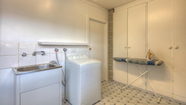 Un área de lavandería con lavadora, lavabo y tabla de planchar.