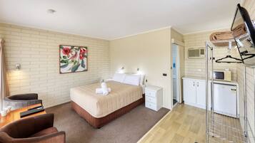A hotel room with a bed, bedside tables, a desk with a chair, a painting on the wall, and a kitchenette with a microwave and refrigerator.