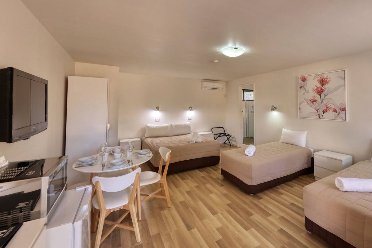 Habitación de hotel con dos camas, una mesa de comedor con sillas, un televisor y zona de ducha.