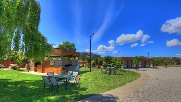 A patio area with a table and chairs, a pergola, and a small building with a brick wall. - Motel Meneres (Corowa)