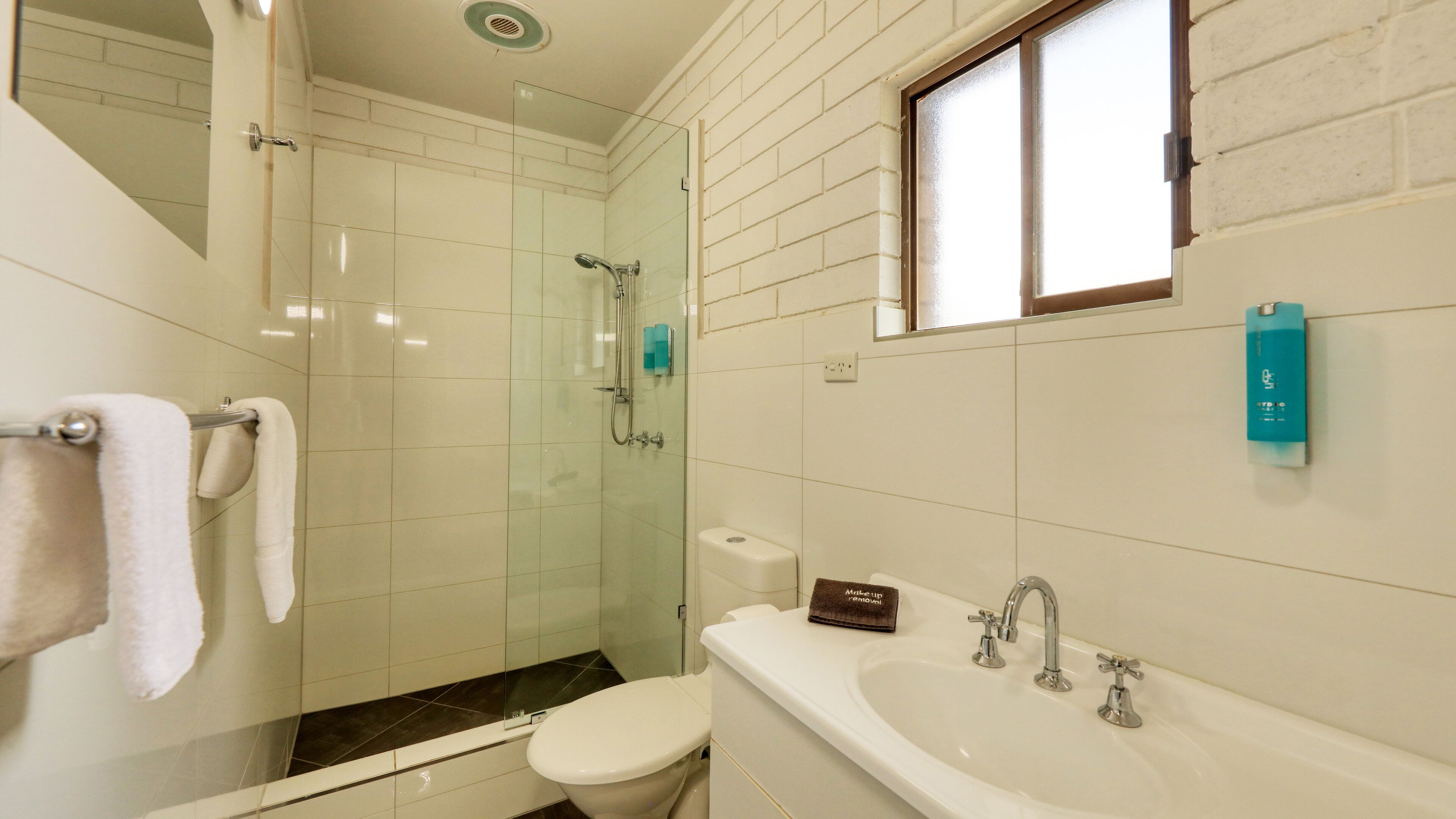 Une salle de bain avec une douche à parois de verre, des toilettes blanches et un lavabo blanc doté de deux robinets.