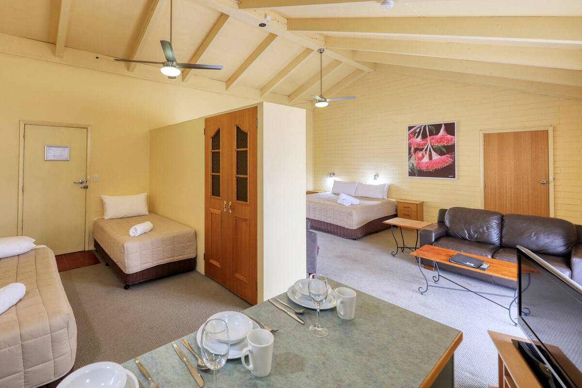 Una habitación de hotel con dos camas, un sofá, una mesa de comedor con cubiertos y un televisor.