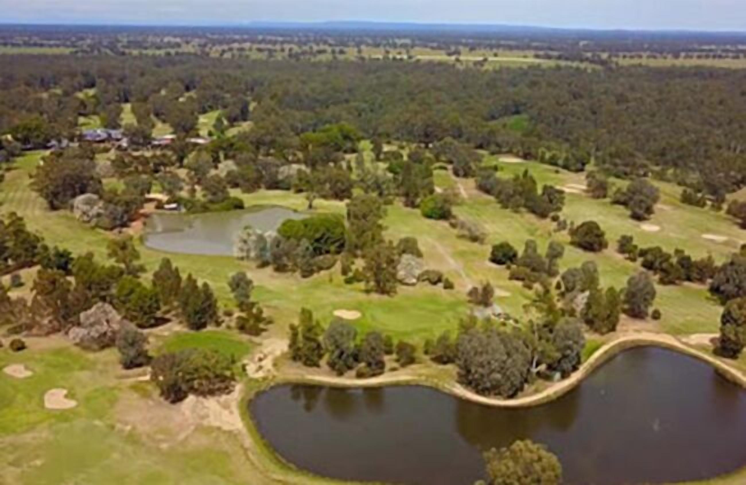 An aerial view of a golf course with multiple ponds, trees, and a few buildings.