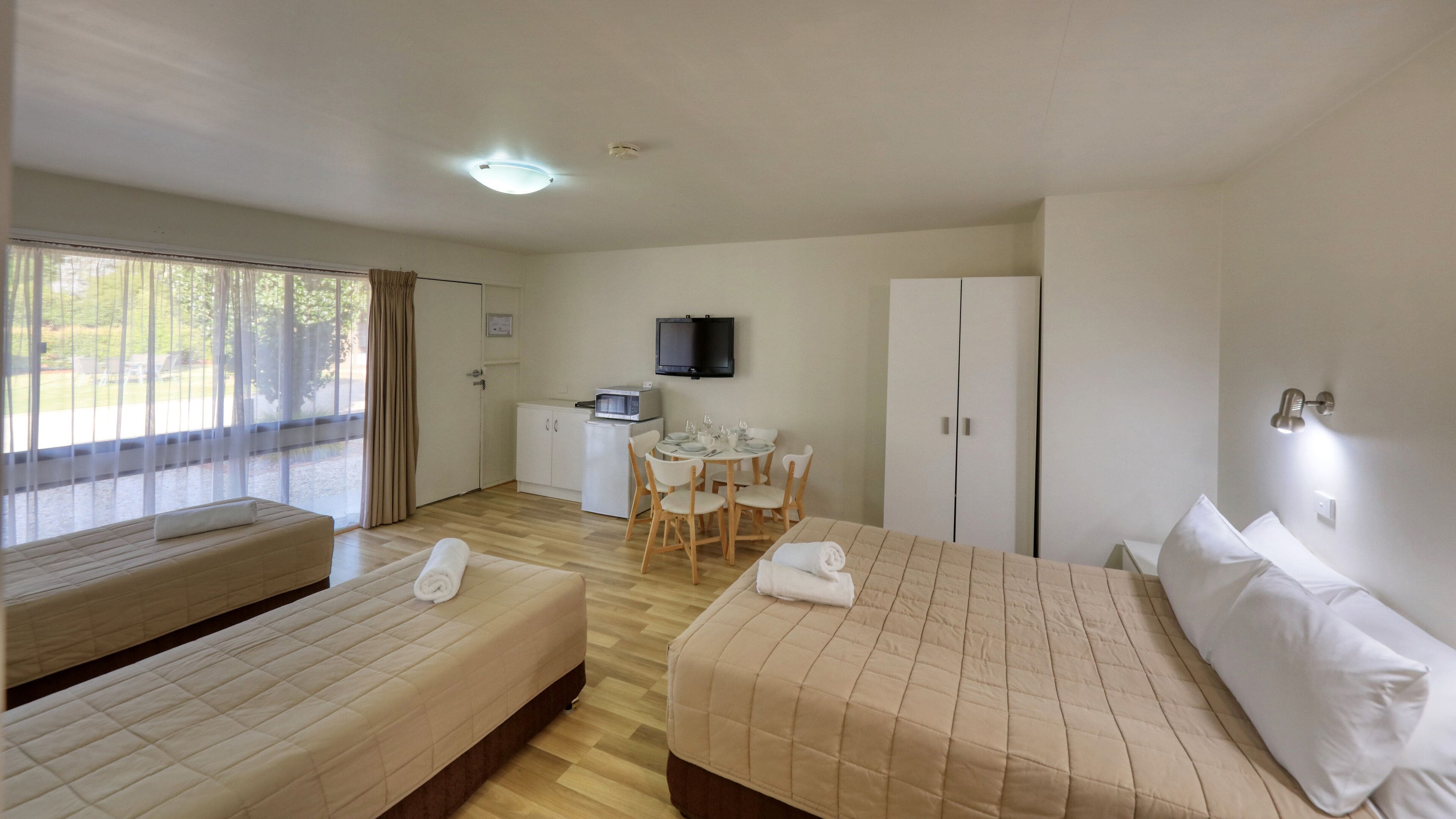 Une chambre d’hôtel avec deux lits, une table à manger avec des chaises, un téléviseur et une armoire.