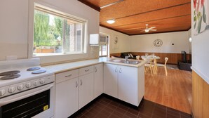 A kitchen with a stove, oven, and sink. There is a dining area with a table and chairs. - Motel Meneres (Corowa)