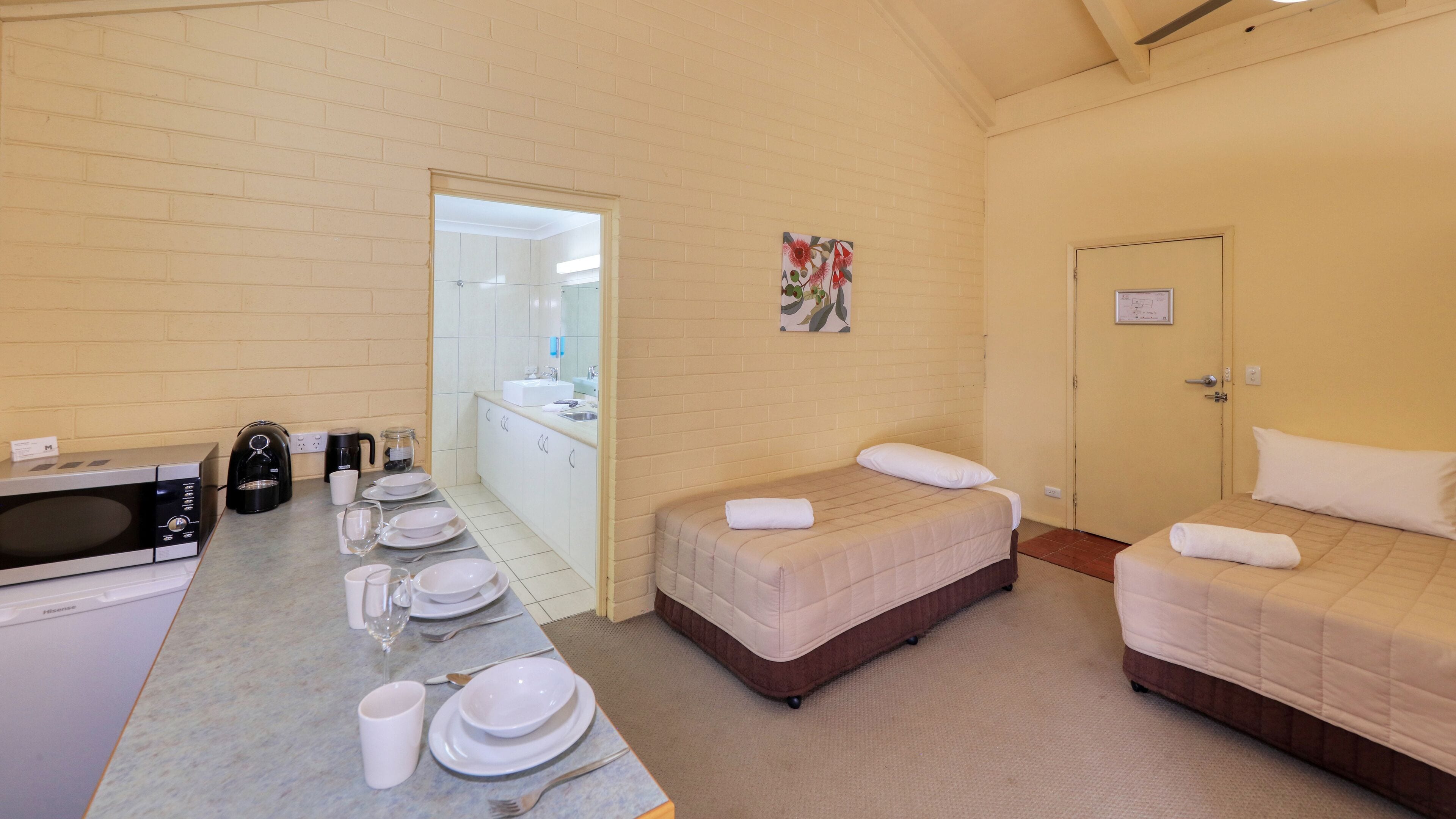 Une chambre d’hôtel équipée d’une kitchenette, de deux lits, d’une salle de bain et d’un coin repas aménagé pour le petit-déjeuner.