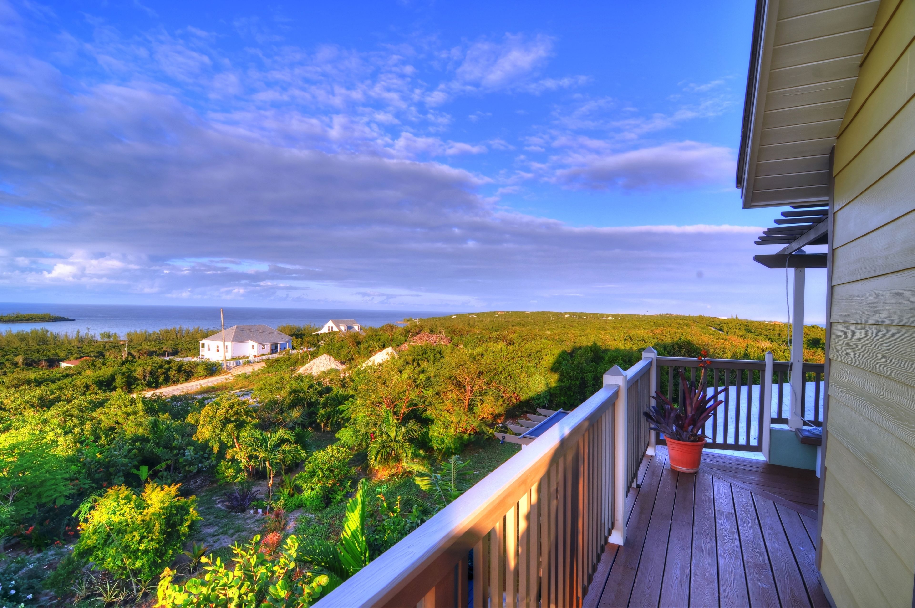 A wooden deck with a railing, overlooking a lush green landscape and a body of water.
