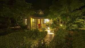 A small, illuminated house surrounded by lush greenery and a wooden pathway leading to it. - Villa Allamanda (Governor's Harbour)