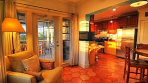 A cozy living room with a sofa, a television, and a kitchen area with wooden cabinets and a refrigerator. - Villa Allamanda (Governor's Harbour)