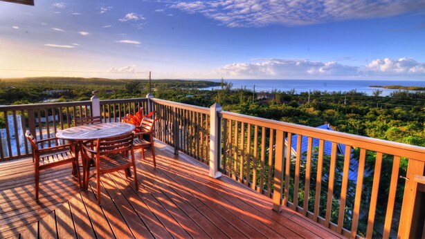 A wooden deck with a table and chairs, overlooking a lush landscape and a body of water. - Villa Allamanda (Governor's Harbour)