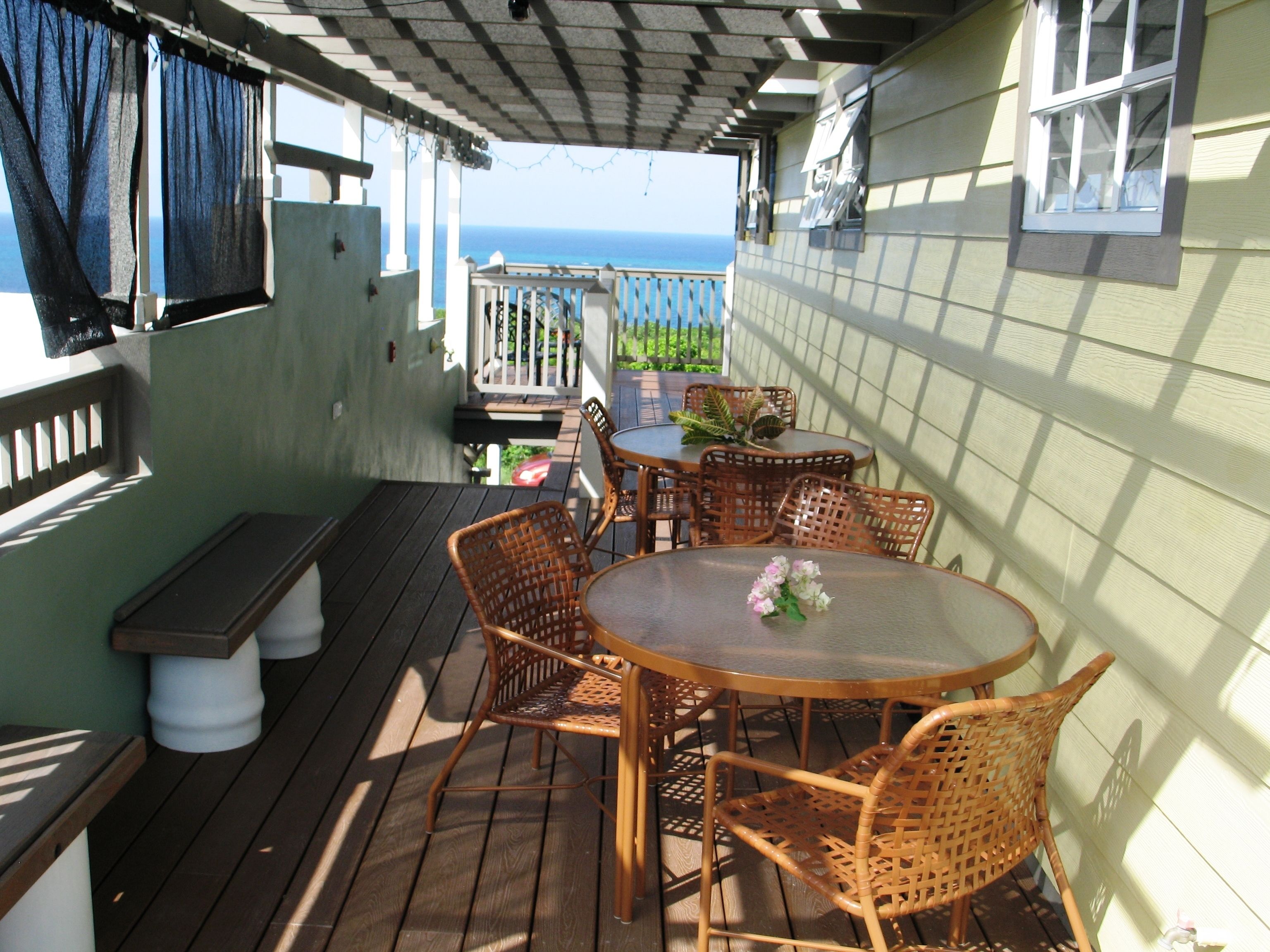 A covered outdoor patio with wooden furniture and a view of the ocean.