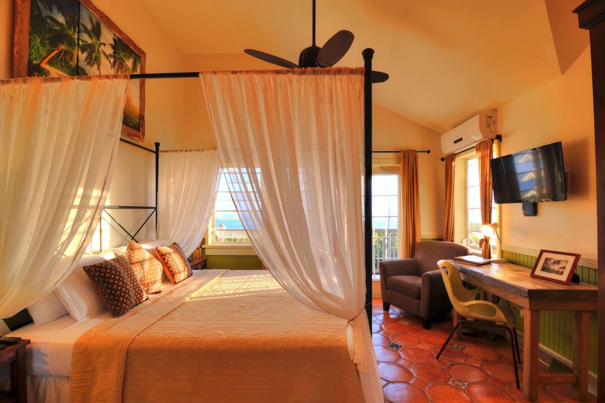 A bedroom with a bed, a desk, a chair, a television, and a window with curtains.