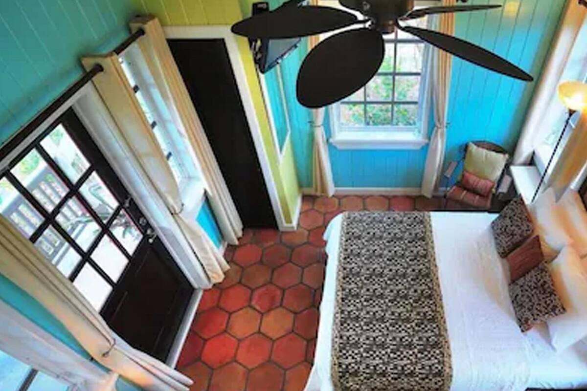 A room with a bed, a ceiling fan, a window, and a door.