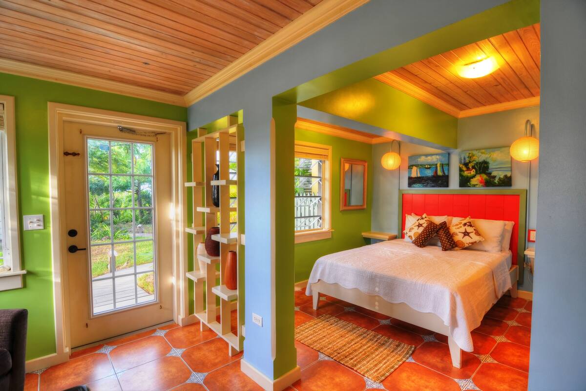 A bedroom with a bed, a wooden ceiling, a green wall, and a window.