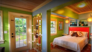 A bedroom with a red headboard, a white bedspread, and a view of the outdoors through a window. - Villa Allamanda (Governor's Harbour)