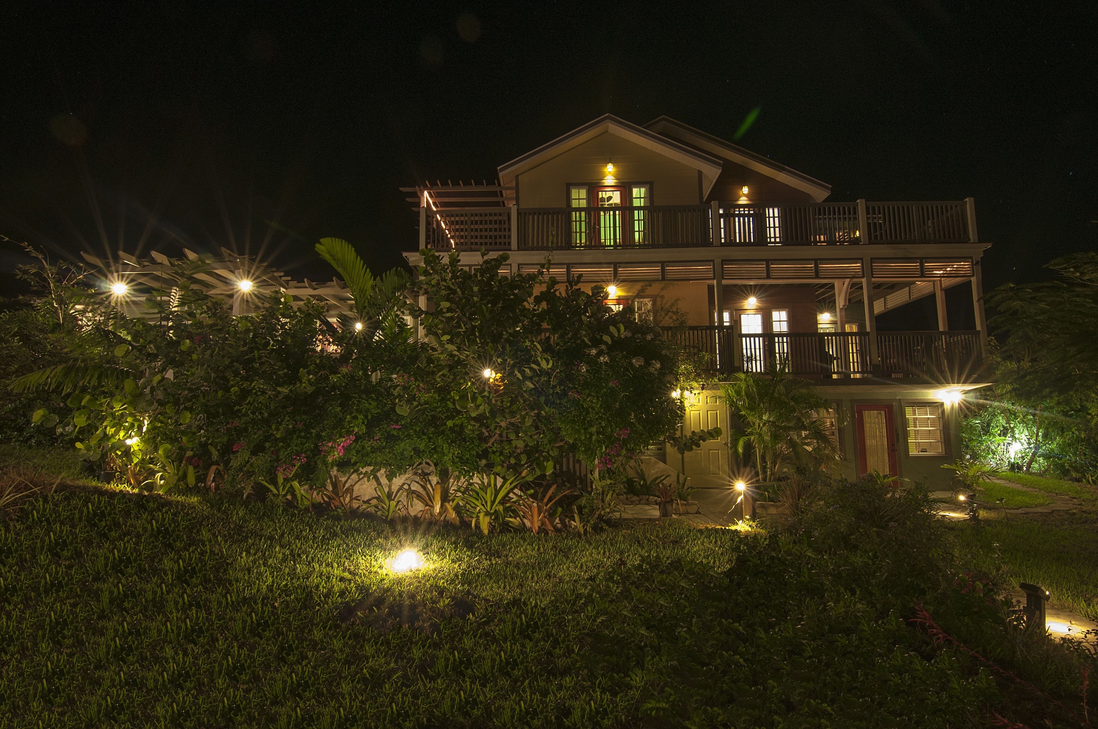 Uma casa de dois andares com varanda e um jardim bem iluminado à noite.