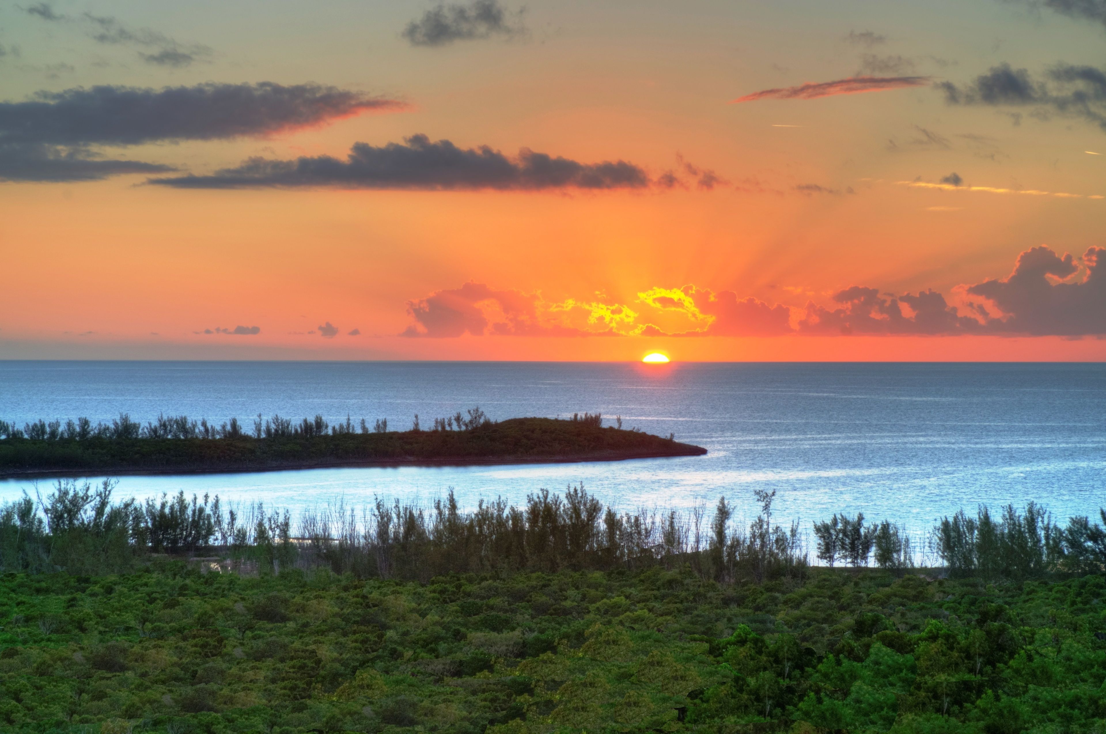 Ein Sonnenuntergang über einem ruhigen Meer mit einer kleinen Insel im Vordergrund.