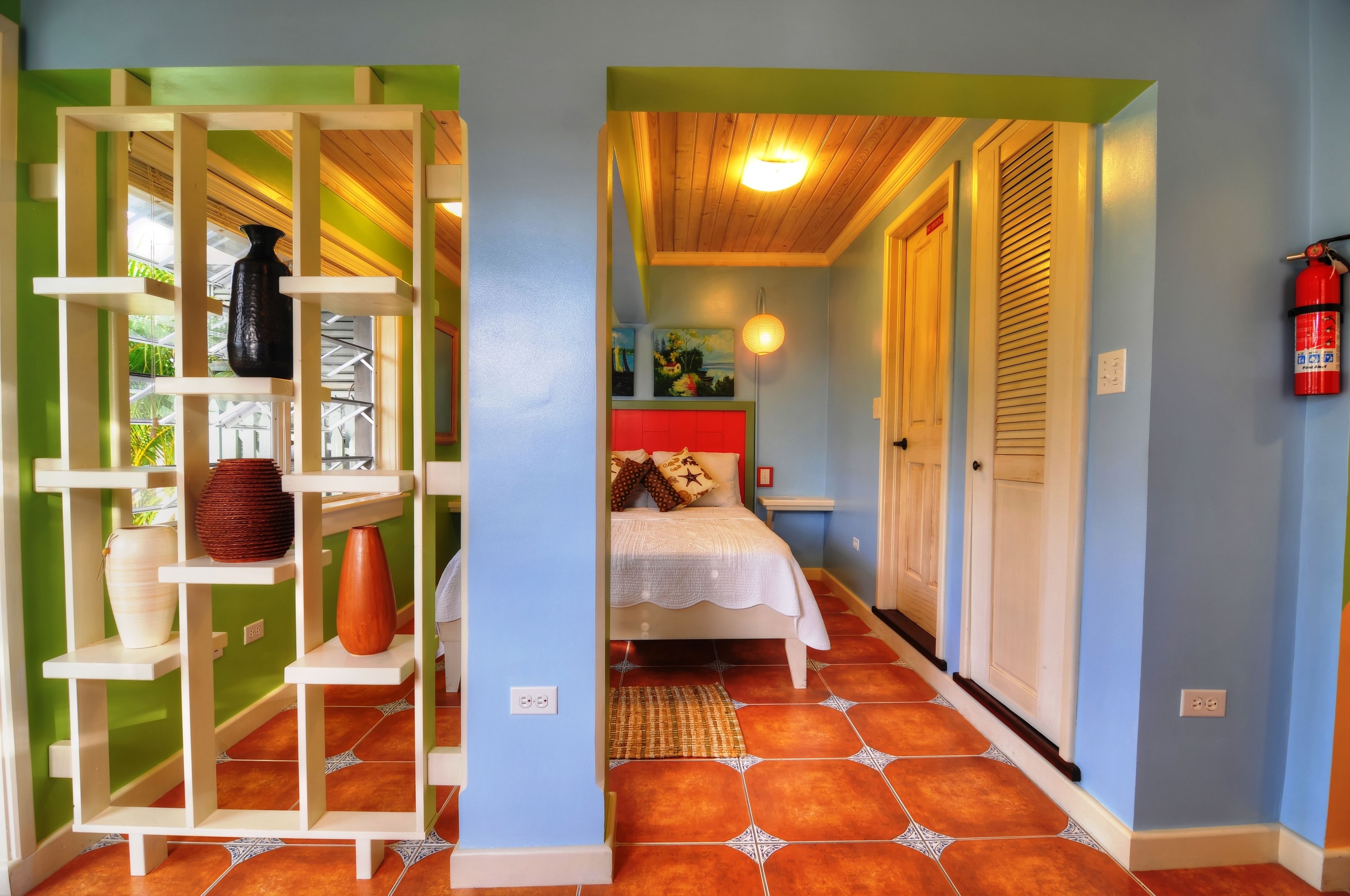 A hallway with a bed, a shelf with decorative items, and a fire extinguisher on the wall.