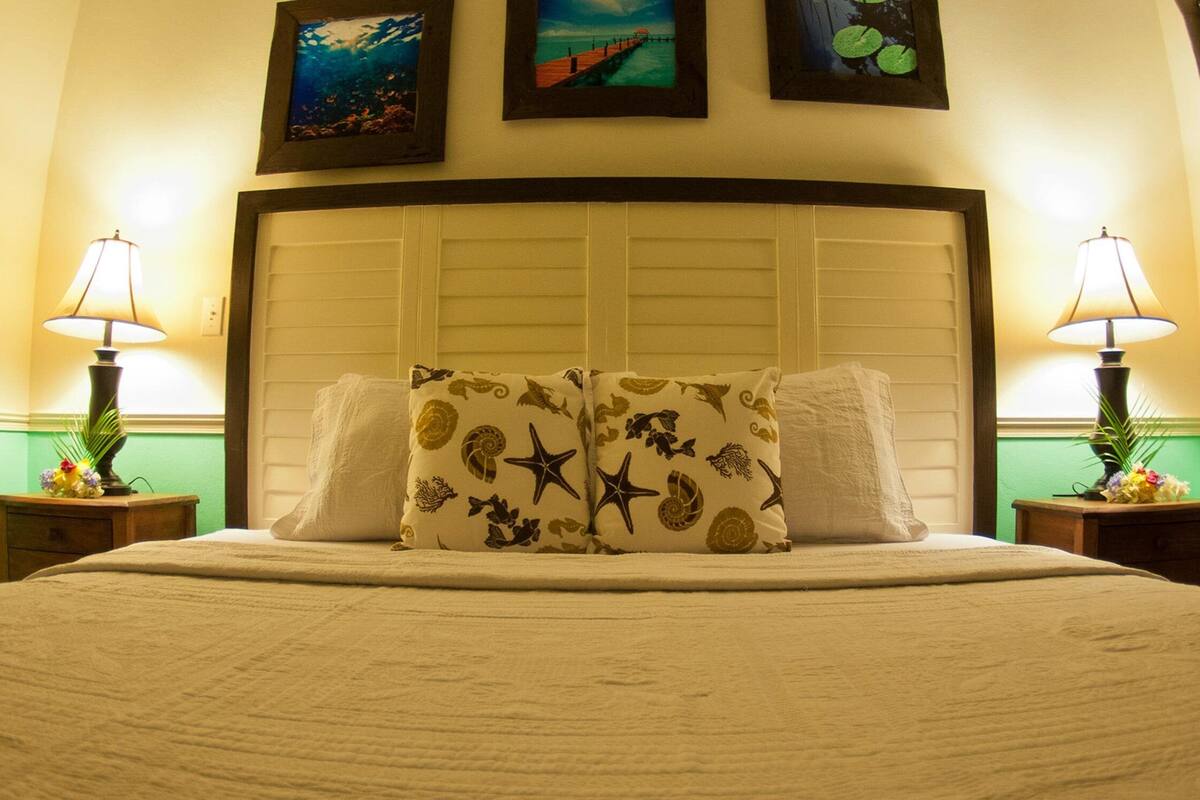 A neatly made bed with a patterned pillow, two bedside lamps, and framed pictures on the wall.